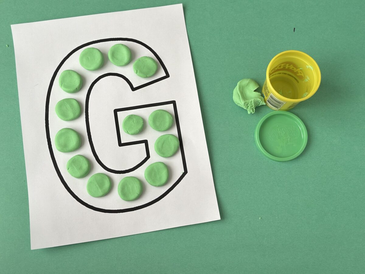 Green playdough squished in circles on a large letter G worksheet. Letter g craft from ABCmouse.com.