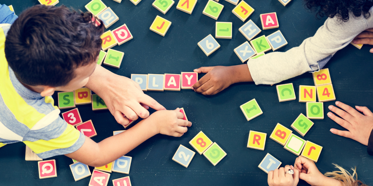 Children playing with letter blocks on the floor. The word play being spelled. 