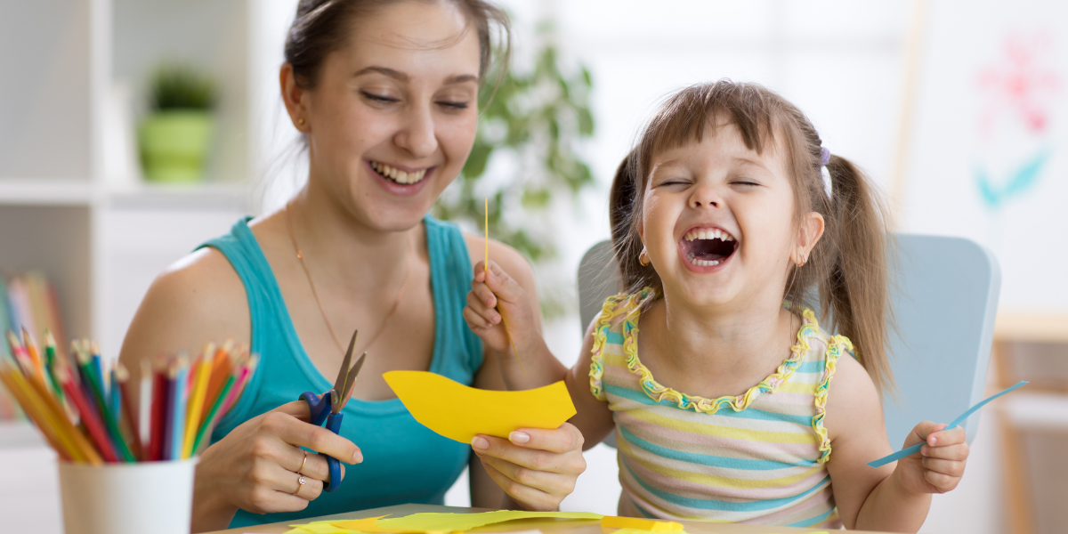 A very happy mother and daughter cutting construction paper. 