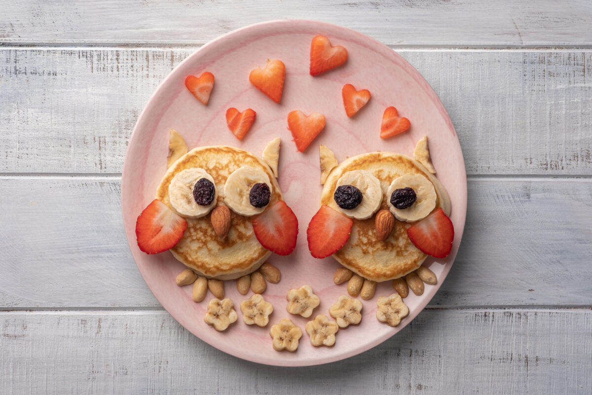 A cute snack made from shapes of food like round pancakes and heart shaped strawberries to for the images of two owls side by side. 