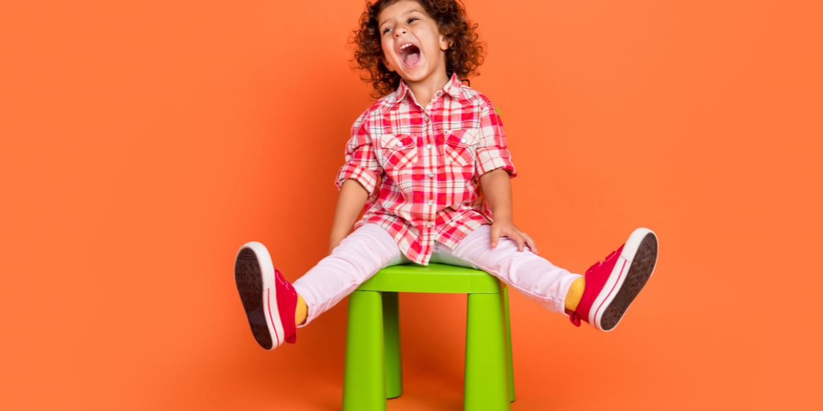 A young boy sitting on a bright green chair with a big smile on his face. 