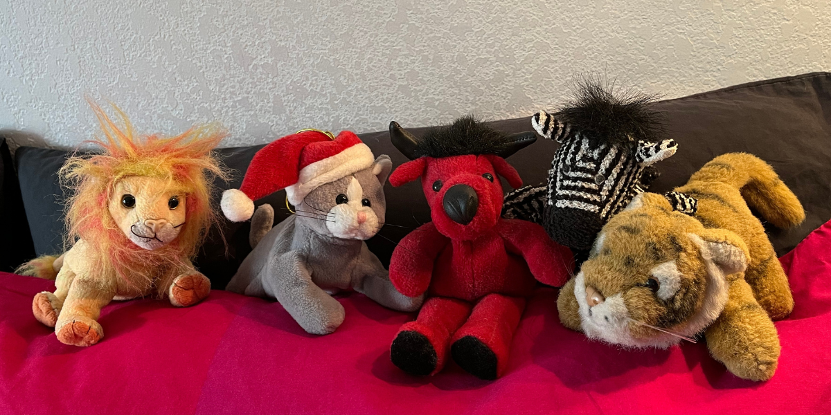 A line of cute stuffed animals sitting on a red couch. 