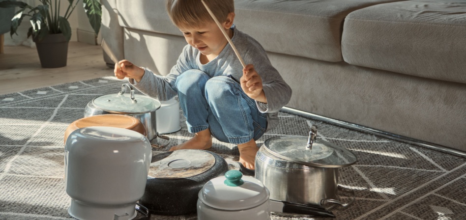 A young boy playing drums on pots and pans on the living room floor. 