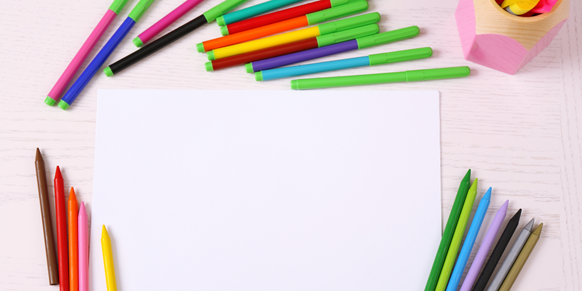 A white piece of paper surrounded by markers and colored pencils. 