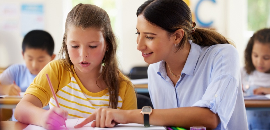 A teacher helping her student who is writing in a notebook. 