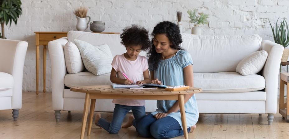 A mother helping her daughter write spelling words in her notebook.