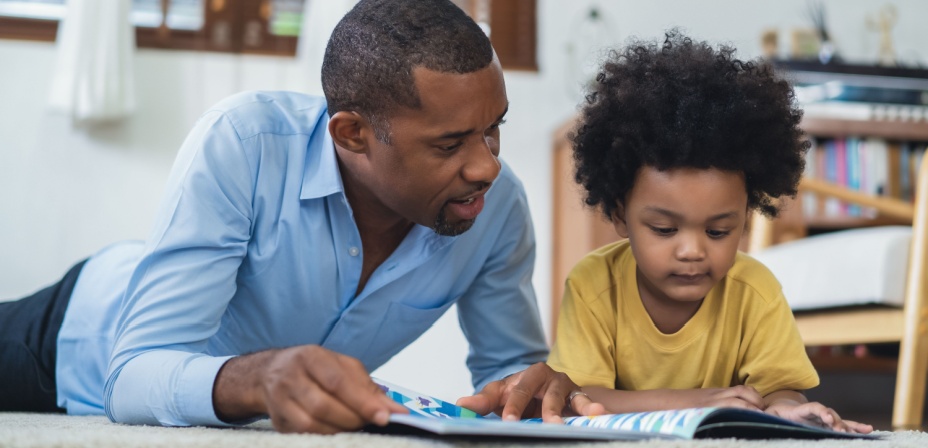 A father reading to his young son while lying on the floor. 