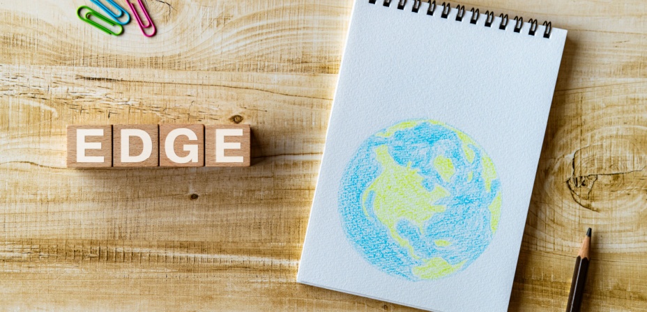 The word edge in wood blocks on a table next to a notebook with a map of the world colored in crayons. 