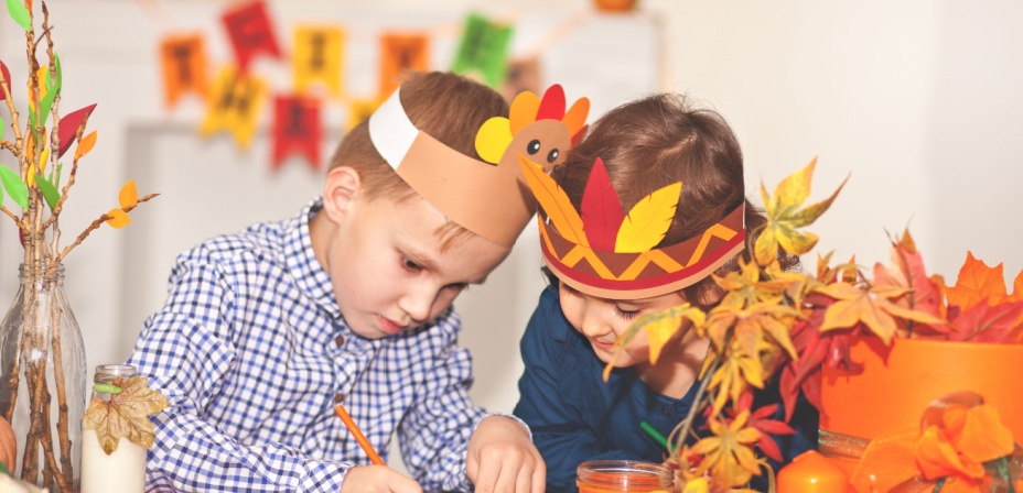 Two children wearing fun thanksgiving head dresses doing thanksgiving activities together. 