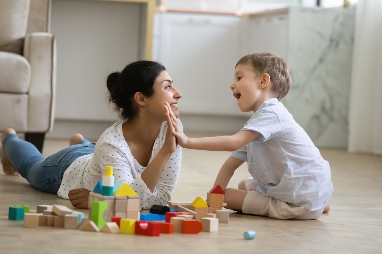 A mom sitting on the floor, playing with blocks with her young son, smiling and giving him a high five.