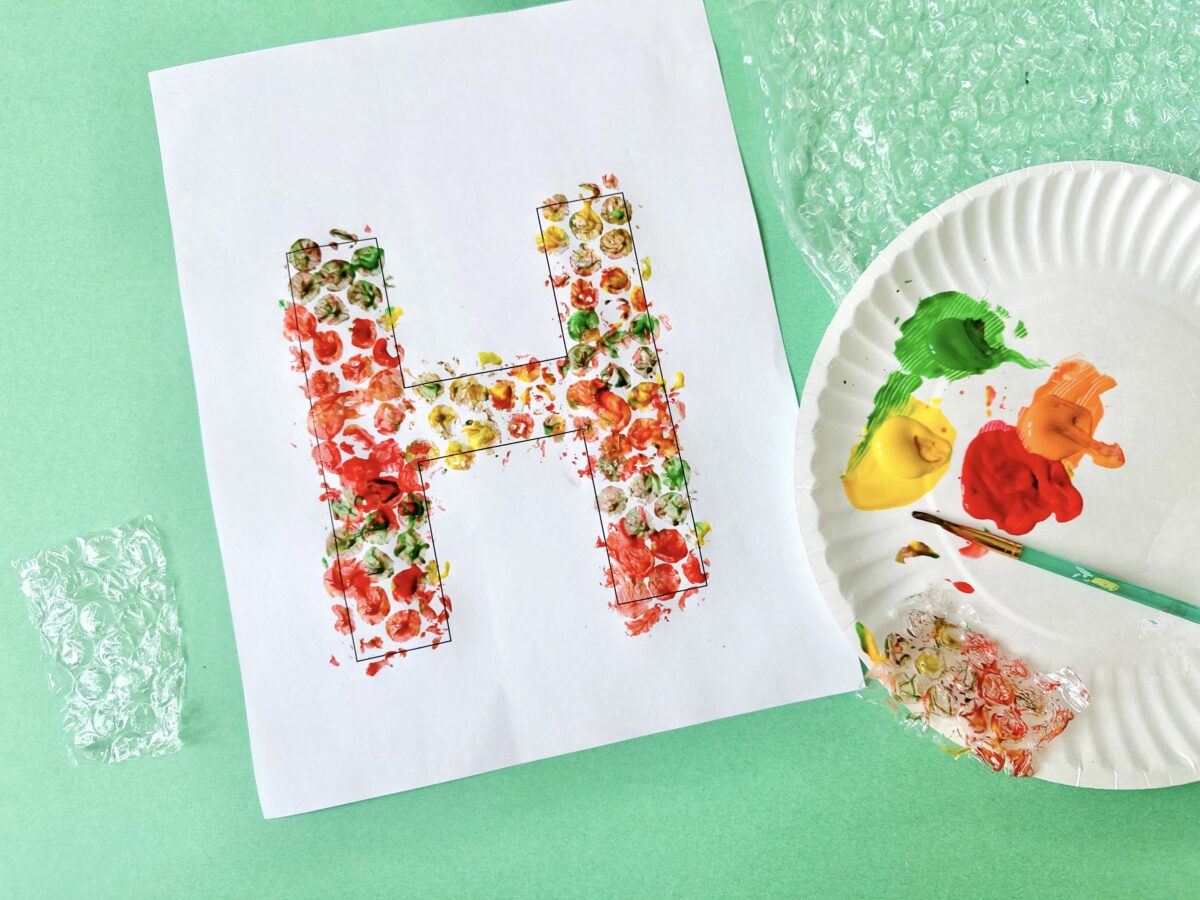 A large letter H painted in fall colors using bubble wrap dipped in paint and pressed on the sheet. 