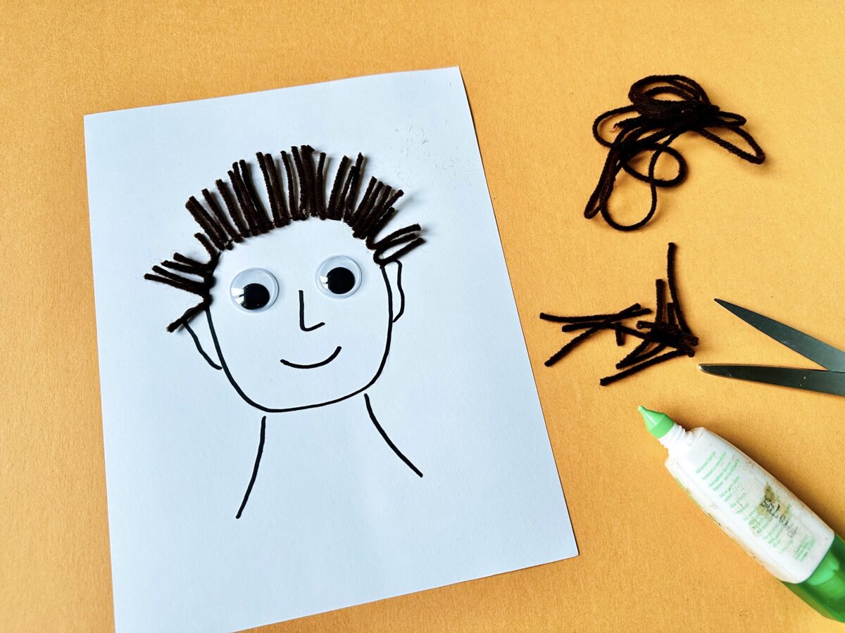 H is for hair fun craft of a face drawn on paper with yarn hair and big google eyes. 