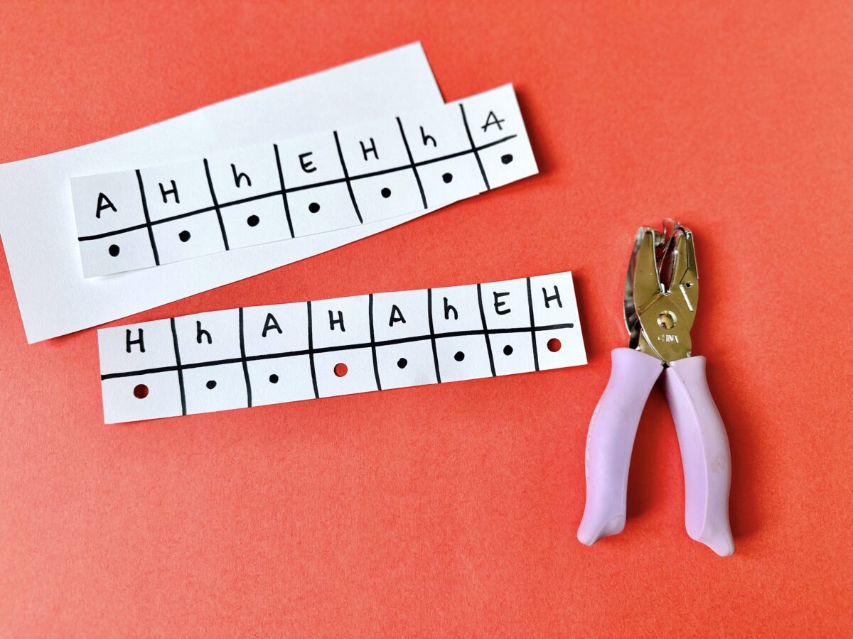 A strip of paper with letters written on it. Children use a holepunch to punch underneath the letter h. 