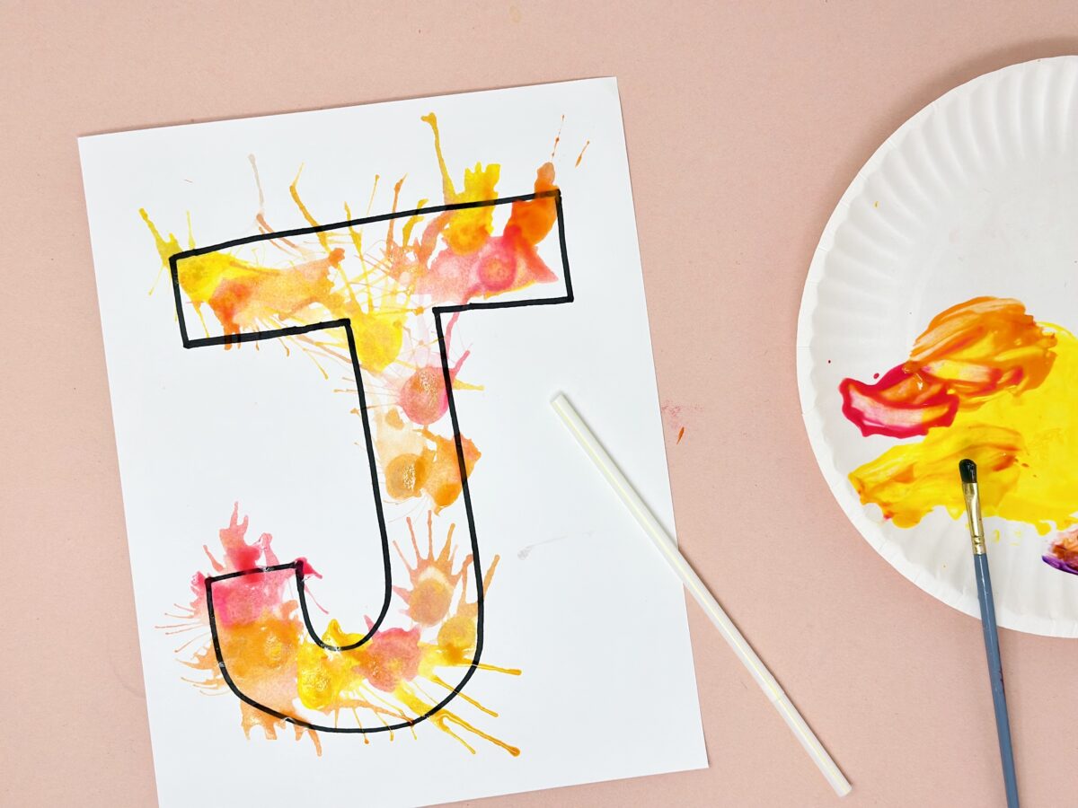 A big letter J on white paper painted by water colors and blowing through a straw. 