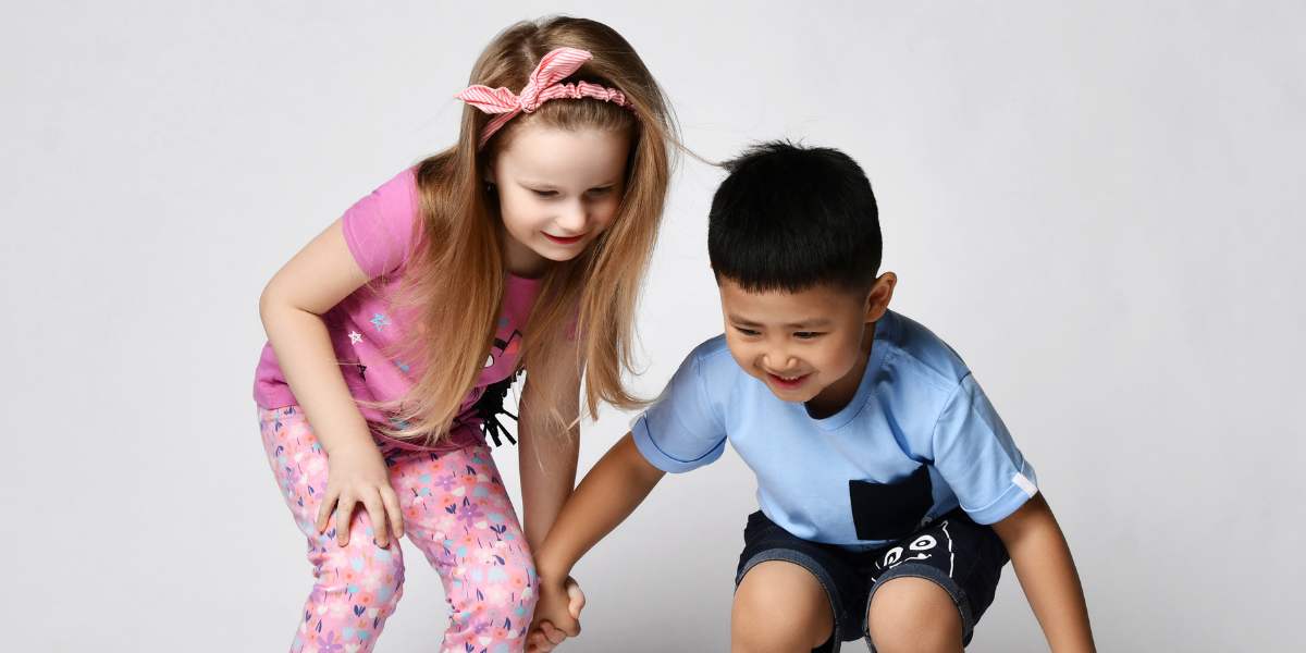 Two happy young children squatting down toward the ground. 