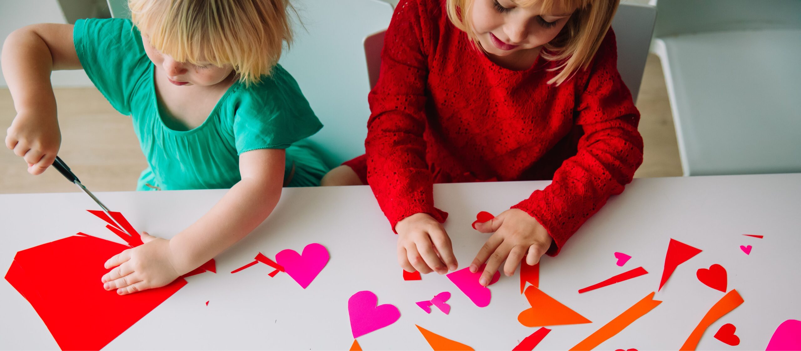 Two young girls cutting paper heart from brightly colored paper. 