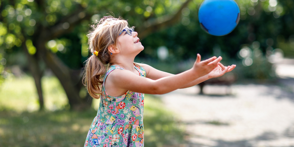 A young preschool age girl catching a blue ball. 