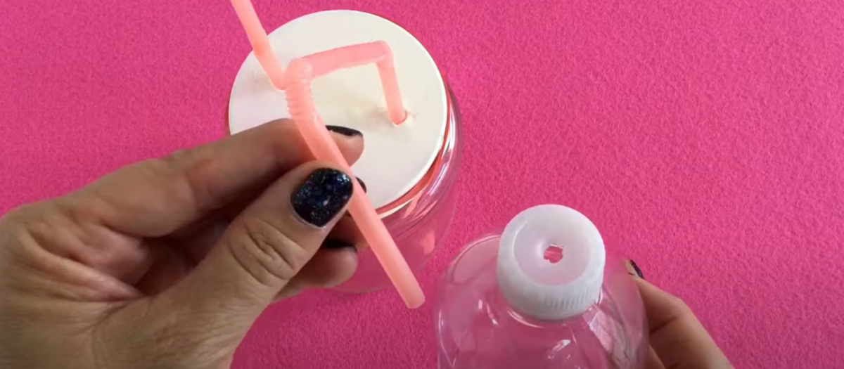 A small plastic water bottle with a hole in the top and a glass jar covered with a white balloon and straws coming out for this STEM model heart project for kids. 