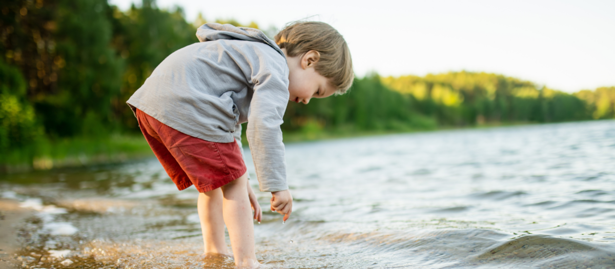 A young boy walking around a lake shore exploring. 