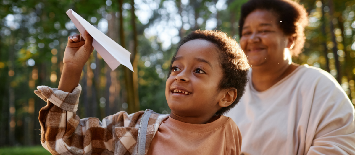 A young boy smiling as he is throwing a paper airplane. 