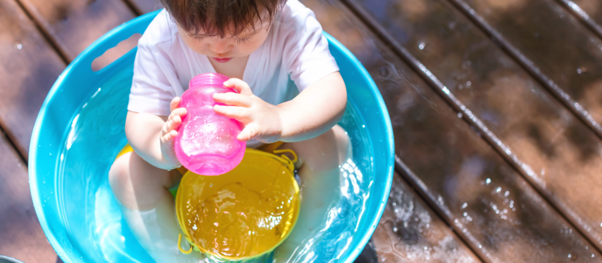 Young child playing with containers and water in a very small pool. 