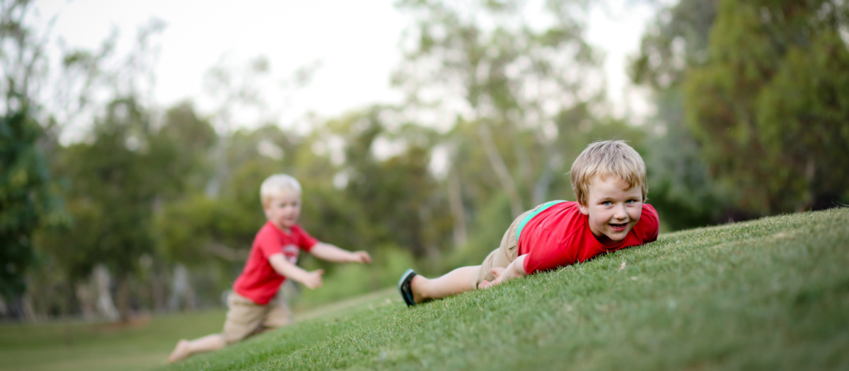 Two young boys having fun rolling down a green grassy hill. 