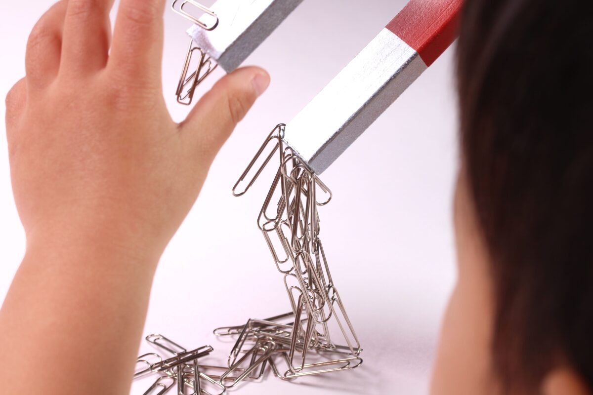 A child playing with a large magnet and paper clips. 