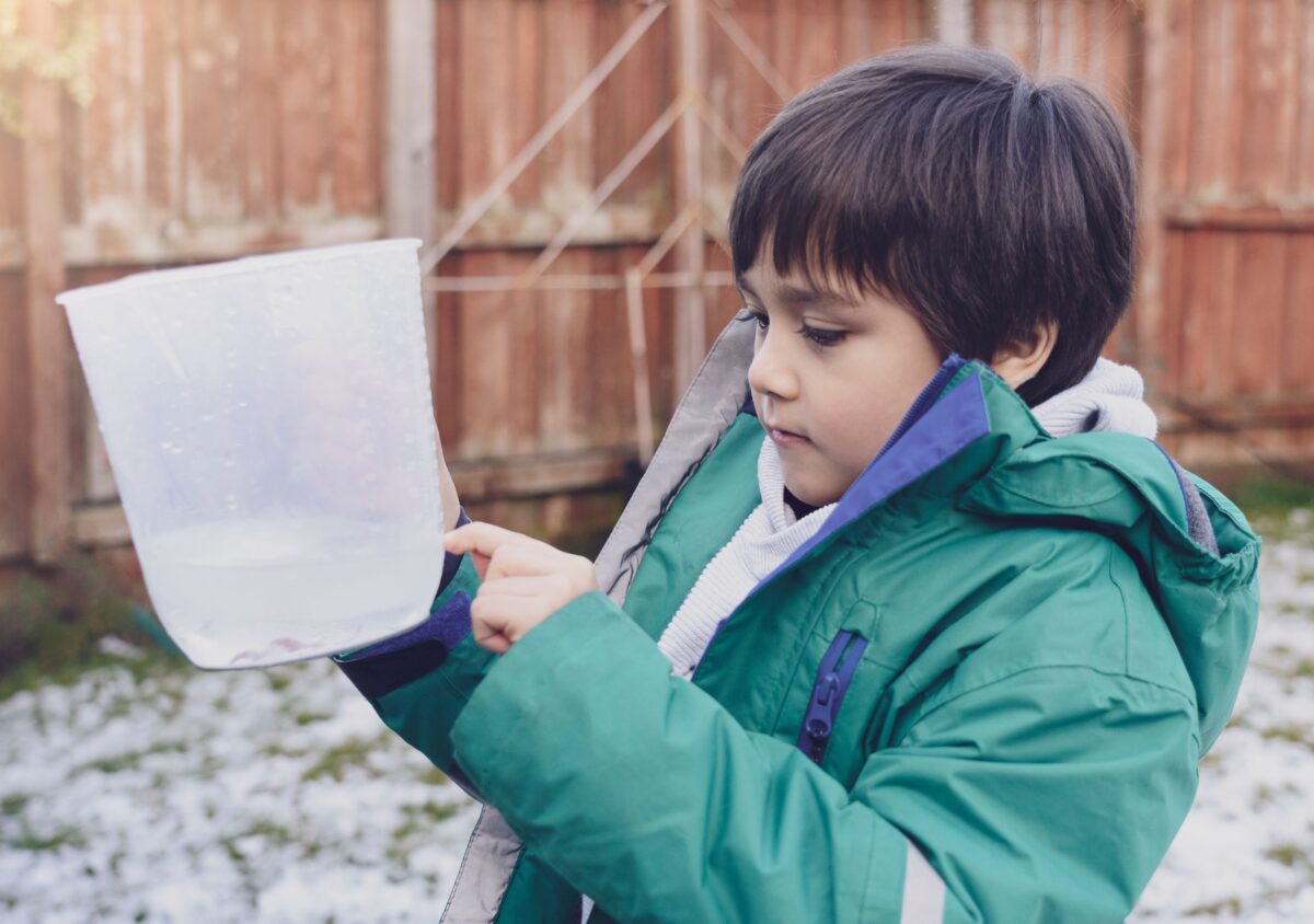 A child measuring rain water in a measuring cup. 