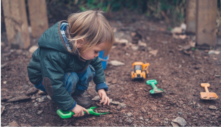 Small child shoveling dirt and playing. 