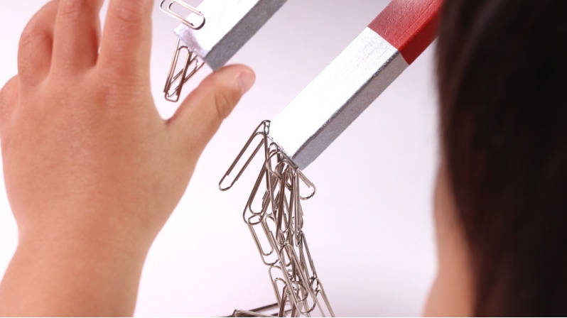 A child playing with a magnet and paper clips. 