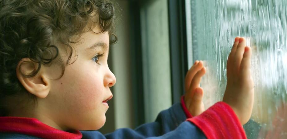 A young child looking out a textured window. 