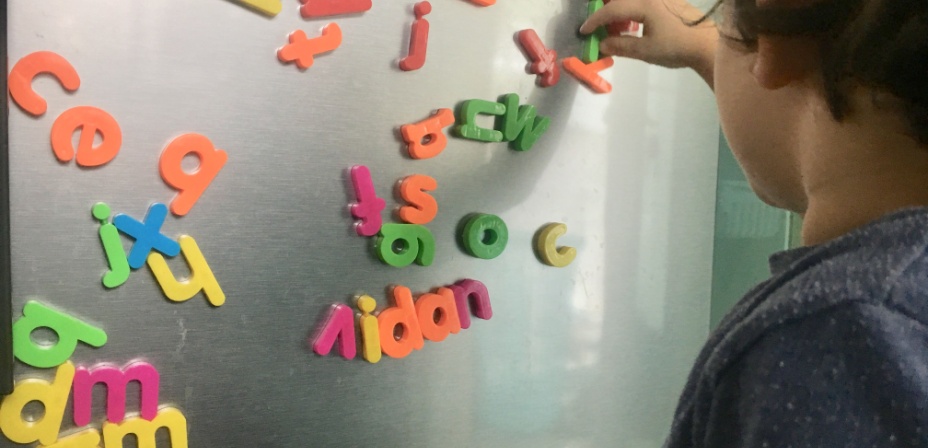 A young boy adding colorful letter magnets to the fridge. 