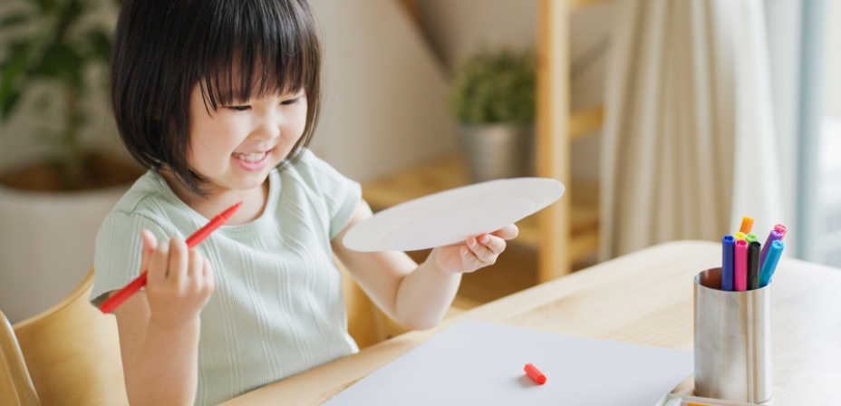 A young girl holding a red marker and smiling 