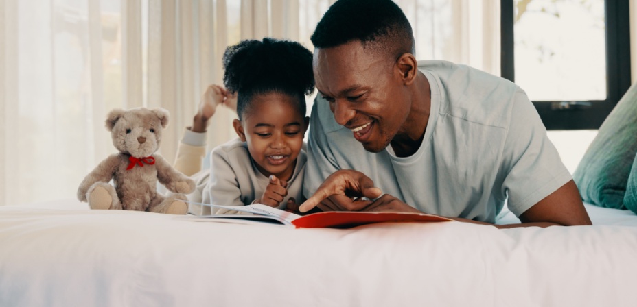 A young girl with her father on the bed reading together. 