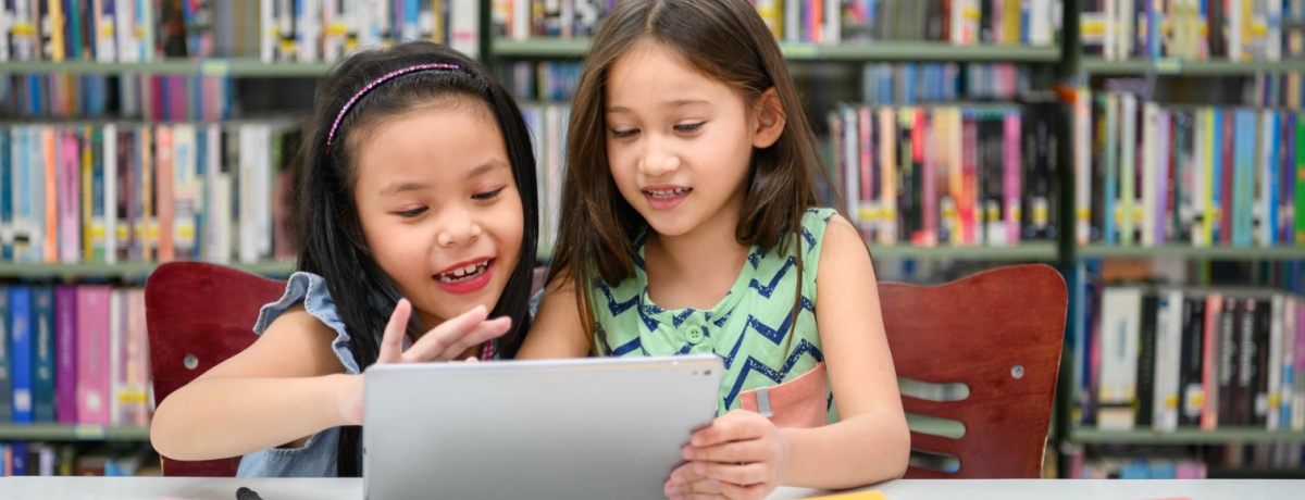 Two girls playing ABCmouse on an i-pad in the library. 