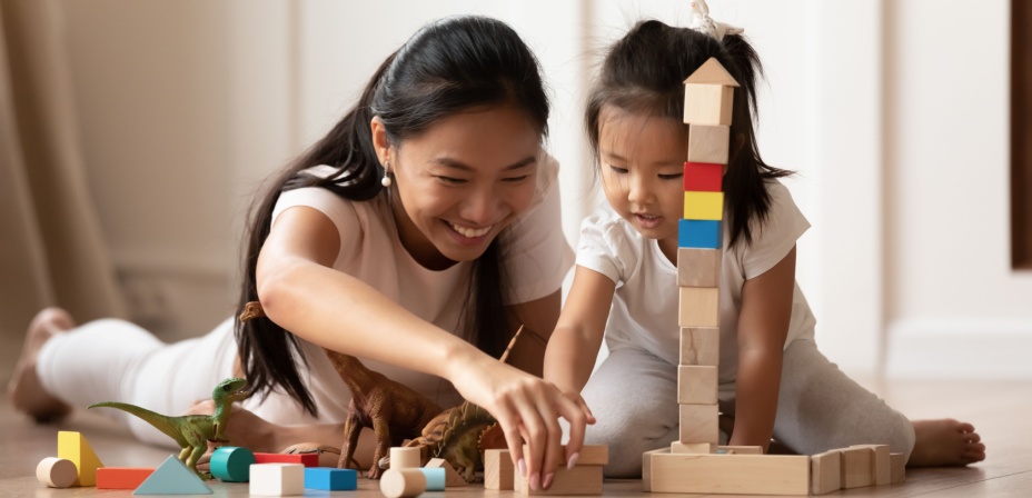 A mother and young daughter stacking wooden blocks on top of each other. 