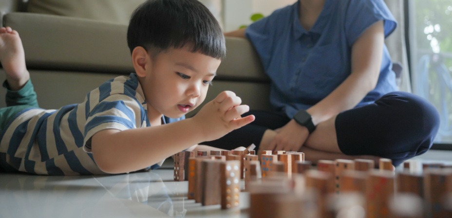 A young boy sitting on the floor lining up dominos in a row to make a chain reaction when they fall. 