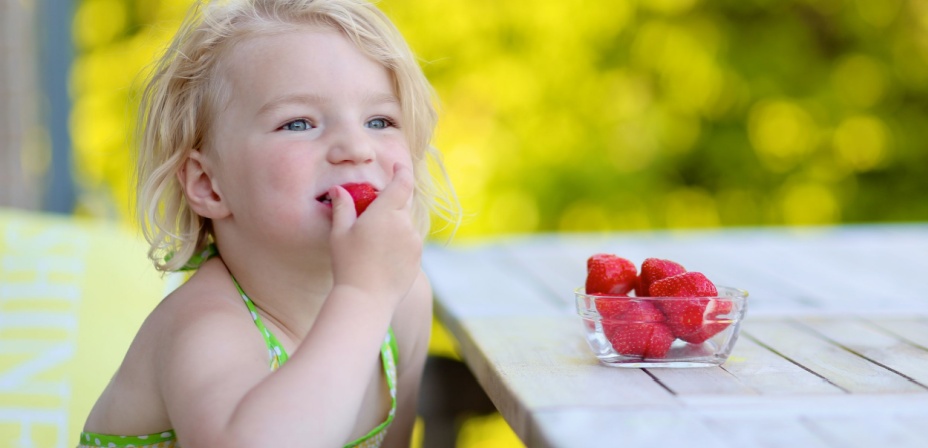 A young blond haired child eating strawberries from a bowl on a nice summer day. 