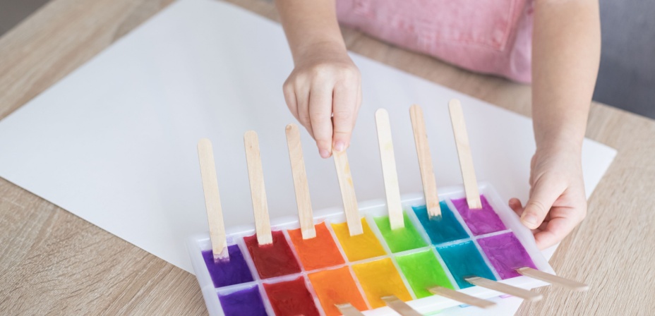 A fun ice painting activity for preschoolers. Colored ice cubes frozen with popsicle sticks coming out. 