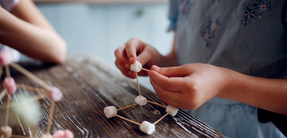 A young child's hands putting a STEM project together with marshmallows and toothpicks. 