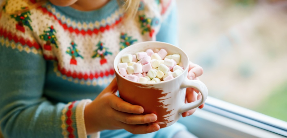 A young child holding a mug of hot cocoa filled with marshmallows. 