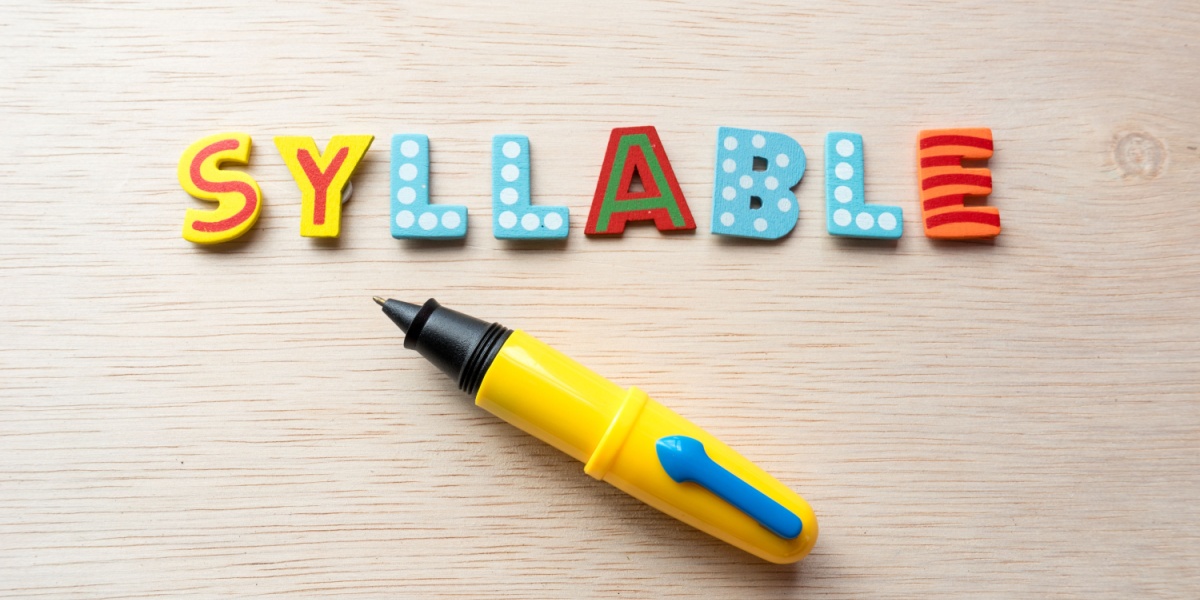 The word syllable in colorful wood letters across a table with a yellow pen underneath. 