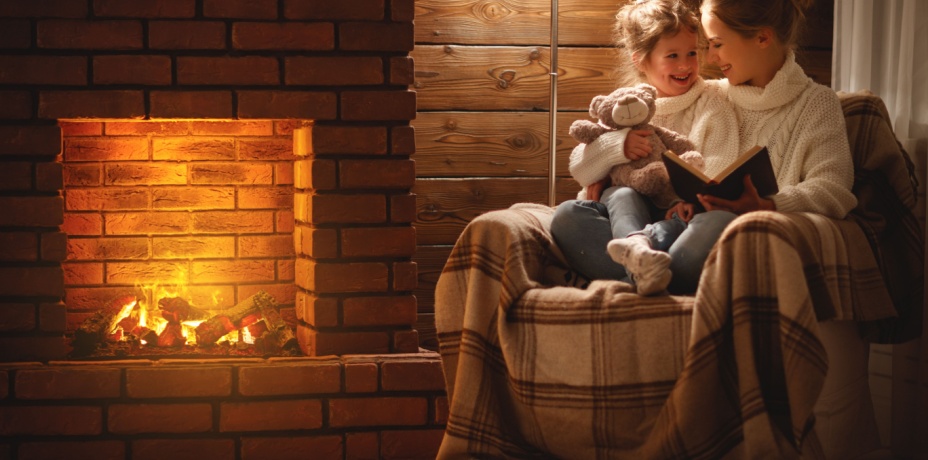 Mother and daughter sitting together in a chair by the fire reading together. 