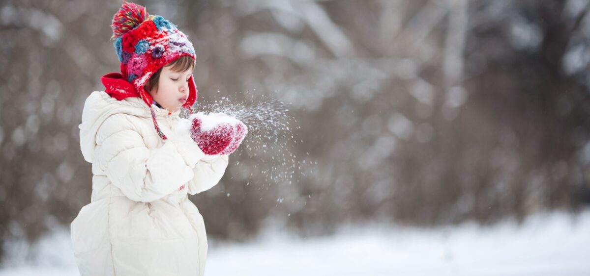 A young child blowing snow out of their hands. 