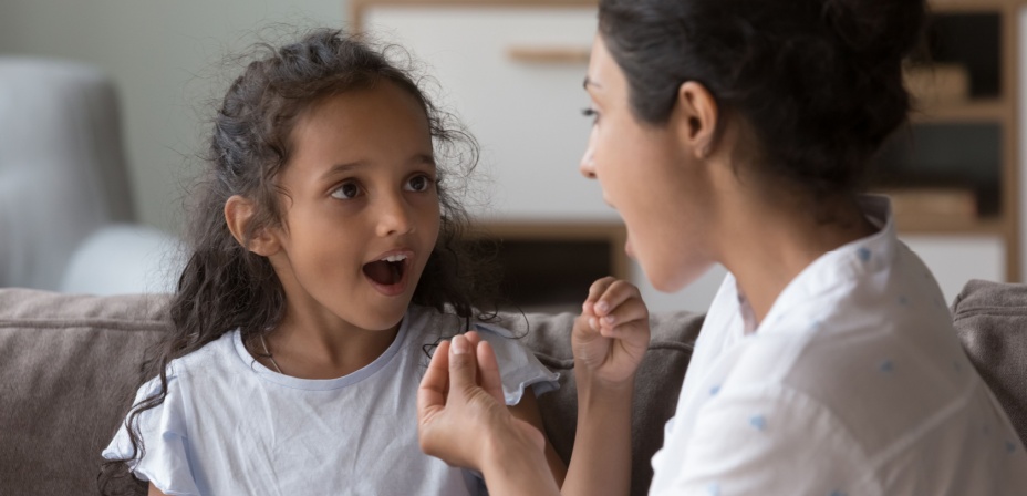 A speech therapist helping a young girl form the sound of words in her mouth correctly. 