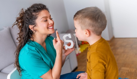 A young mom pointing to her mouth while making the letter S sound to help her son learn how to say it properly. 