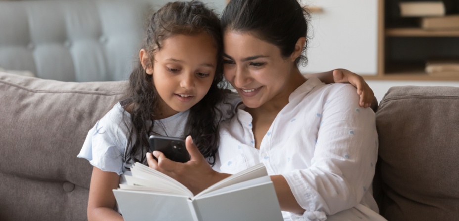 A young mom sitting next to her daughter reading. 