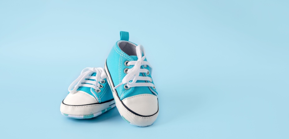 A small pair of toddler sneakers sitting in a light blue background. 