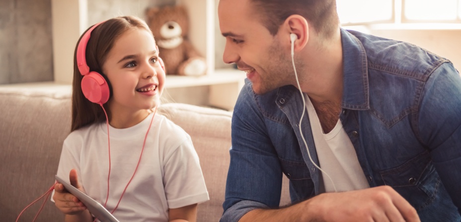 A young girl and her father listening to music together wearing their head phones. 