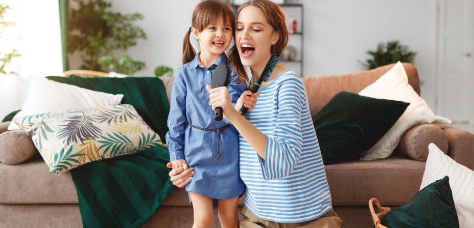 A young mom and her daughter singing into hairbrushes they are holding like a microphone. 